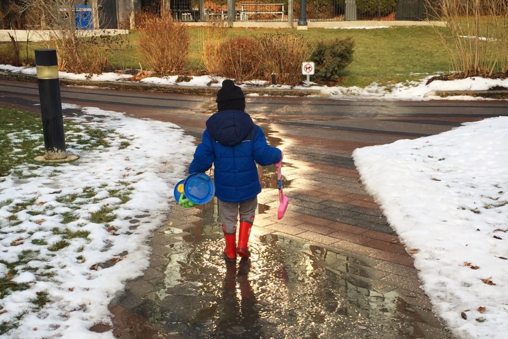 boy wearing a blue jacket walking through the puddle to play in the city of toronto