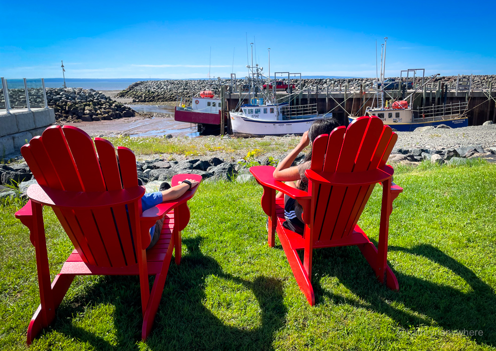 children sitting in Red chairs facing the ocean in the morning light in Alma, New Brunswick