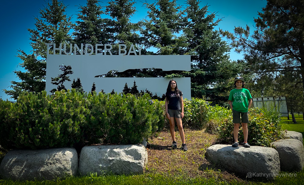 two children standing in front of a Thunder Bay road sign